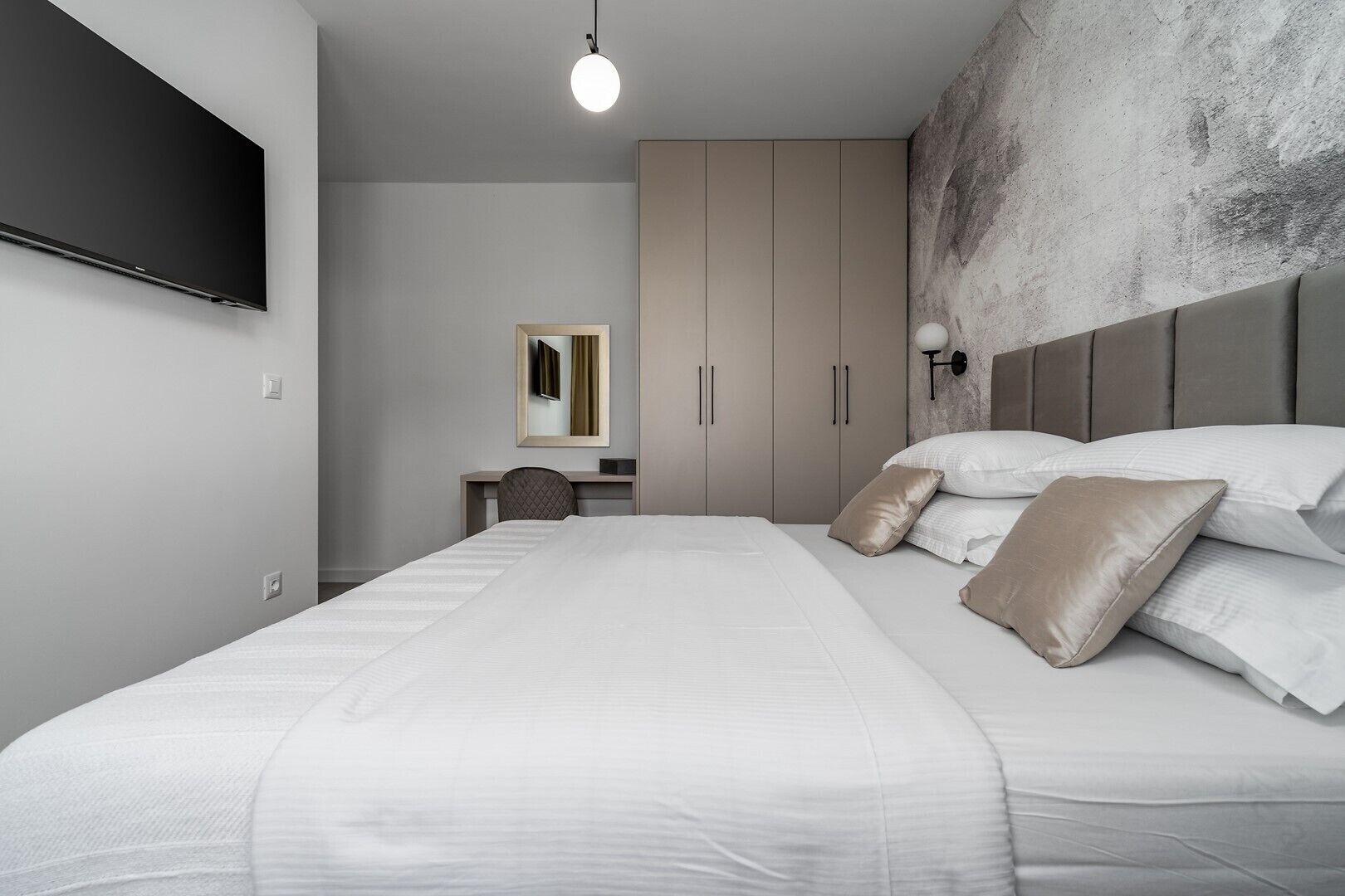 A modern bedroom with a large bed, a desk, a chair, and a wardrobe.
