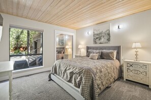 Relax in a serene bedroom with a large bed, nightstand, and dresser, plus a window offering a forest view.