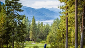Un parcours de golf offrant une vue sur un lac et des montagnes en arrière-plan.