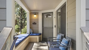 Une véranda avec un banc et deux fauteuils en osier, une porte avec une fenêtre et un luminaire fixé au mur.