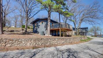 A two-story house with a stone retaining wall, a balcony, and a view of the surrounding trees.