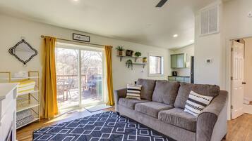 A living room with a sofa, a patterned rug, a dining area with a table and chairs, and a kitchen in the background.