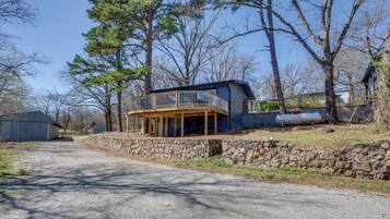 A two-story house with a balcony, a stone retaining wall, and a gravel driveway.