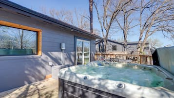 A hot tub in a backyard with a house, a deck, and leafless trees.