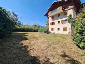 A multi-story building with balconies, a grassy yard, and surrounding trees.