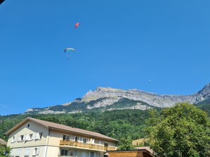 Ein Gebäude mit mehreren Fenstern und Balkonen vor einer Bergkulisse und blauem Himmel.