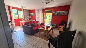 Een woonkamer met een rode wand, een grijze bank, een houten salontafel en een eethoek met een tafel en stoelen.