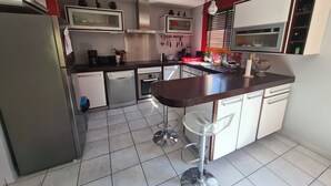 Een compacte keuken met een koelkast, vaatwasser, oven en magnetron. Er staan barstoelen en een kleine eettafel.
