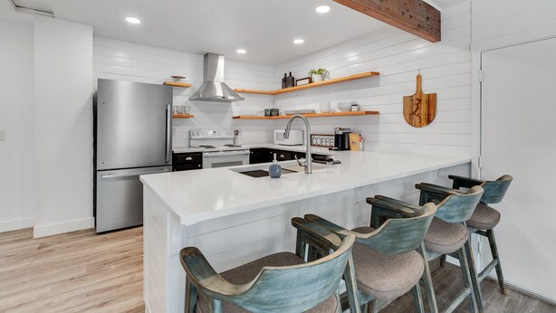 A modern kitchen with white cabinetry, a stainless steel refrigerator, a central island with bar stools, and wooden beams on the ceiling. - CDA ID. Sanders Beach! Best Location! Newly Remodeled Addition! Pet Friendly. (Coeur d'Alene)