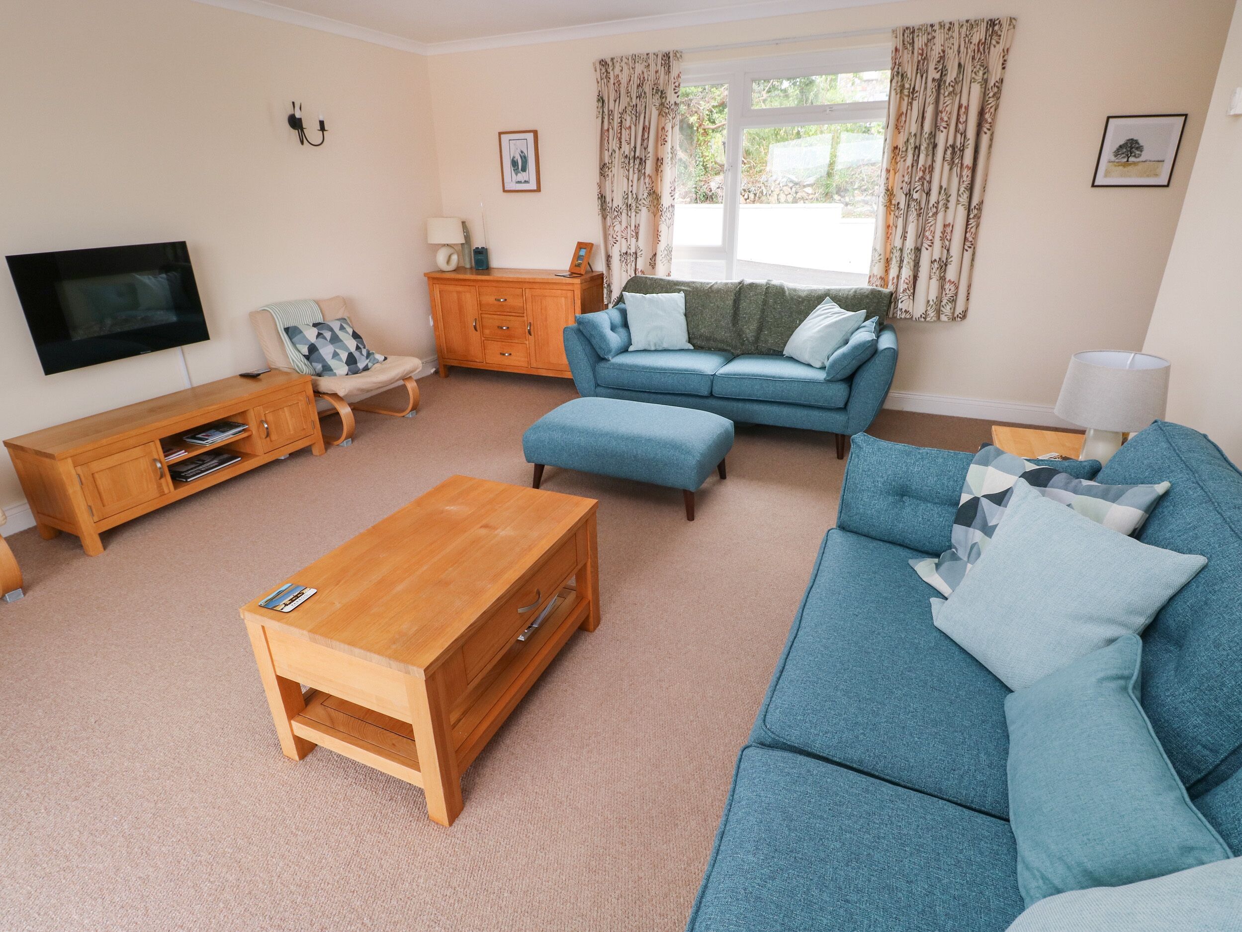 A living room with a blue sofa, wooden coffee table, and a TV on the wall.