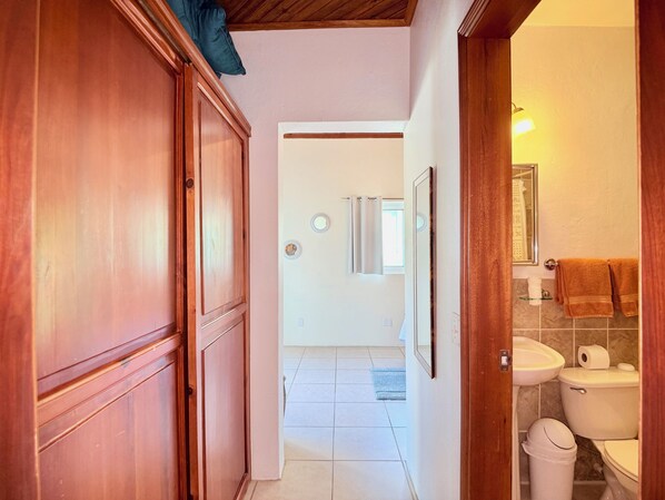 A hallway leading to a bathroom with a toilet, sink, and mirror.