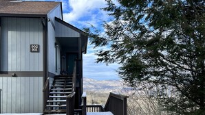 A wooden building with a staircase leading to a porch, surrounded by snow and trees. - Beautiful Sugar Mountain Condo with Long-Range Views (Sugar Mountain)