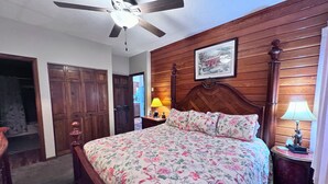 A bedroom with a wooden headboard, a floral bedspread, a ceiling fan, and a nightstand with a lamp. - Beautiful Sugar Mountain Condo with Long-Range Views (Sugar Mountain)
