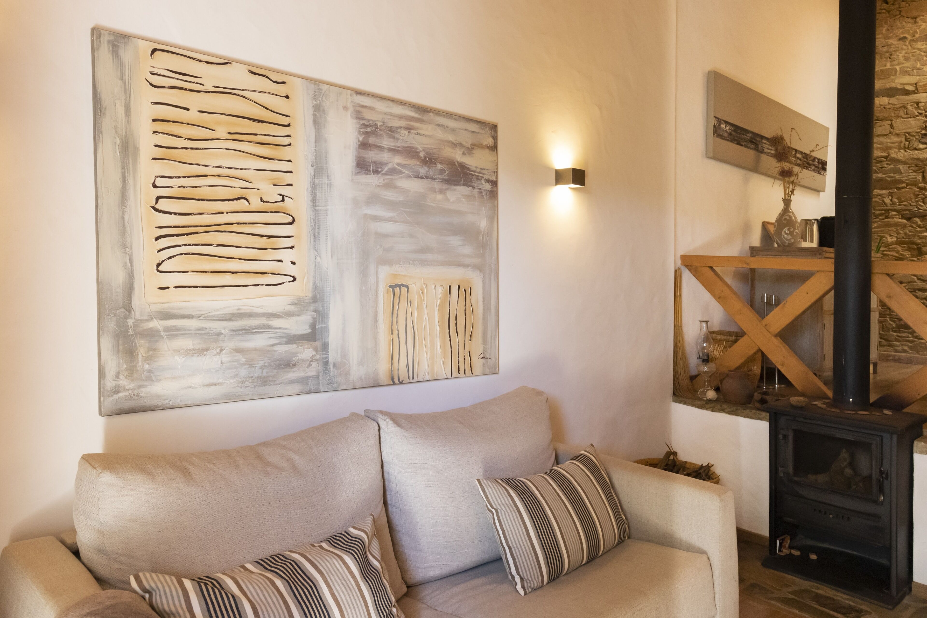 Una sala de estar con un sofá color beige, un cuadro abstracto grande, una pared de piedra y un estufa de leña.