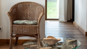 A wicker chair with a cushion, a glass coffee table on a tree stump base, and a woven rug with tassels.