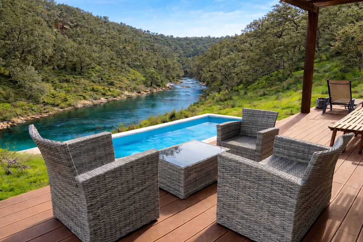 Eine Terrasse mit Korbmöbeln mit Blick auf einen Fluss und bewaldete Hügel.