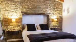 A bedroom with a stone wall, a wooden headboard, two bedside lamps, and a bed with white and dark bedding.