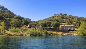 A rustic stone house with a stone bridge, surrounded by lush greenery and a calm lake.