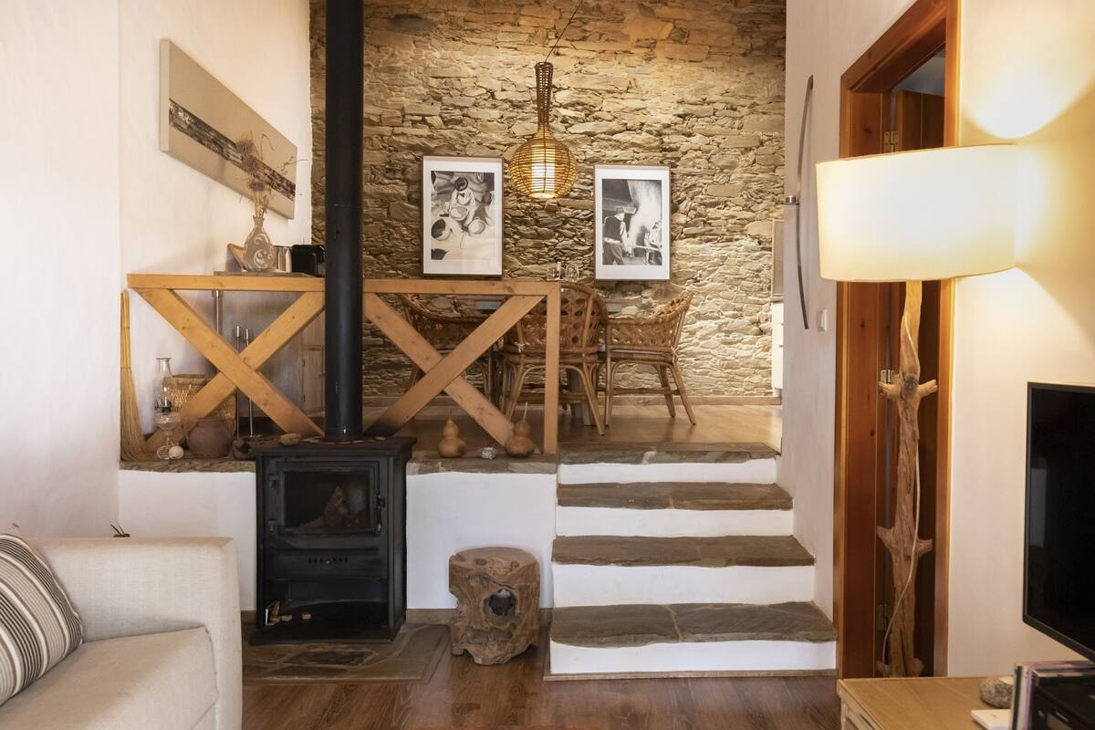 Ein gemütliches Wohnzimmer mit einer Steinwand, einem Kamin, einer Holztreppe und einer Essecke mit Tisch und Stühlen.