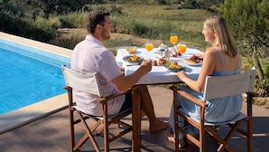 A dining table with a view of a swimming pool and a hill in the background.