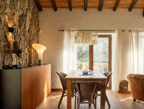 A dining area with a stone wall, wooden ceiling, and a table with chairs. - Casas de Campo do Castro da Cola (Ourique)
