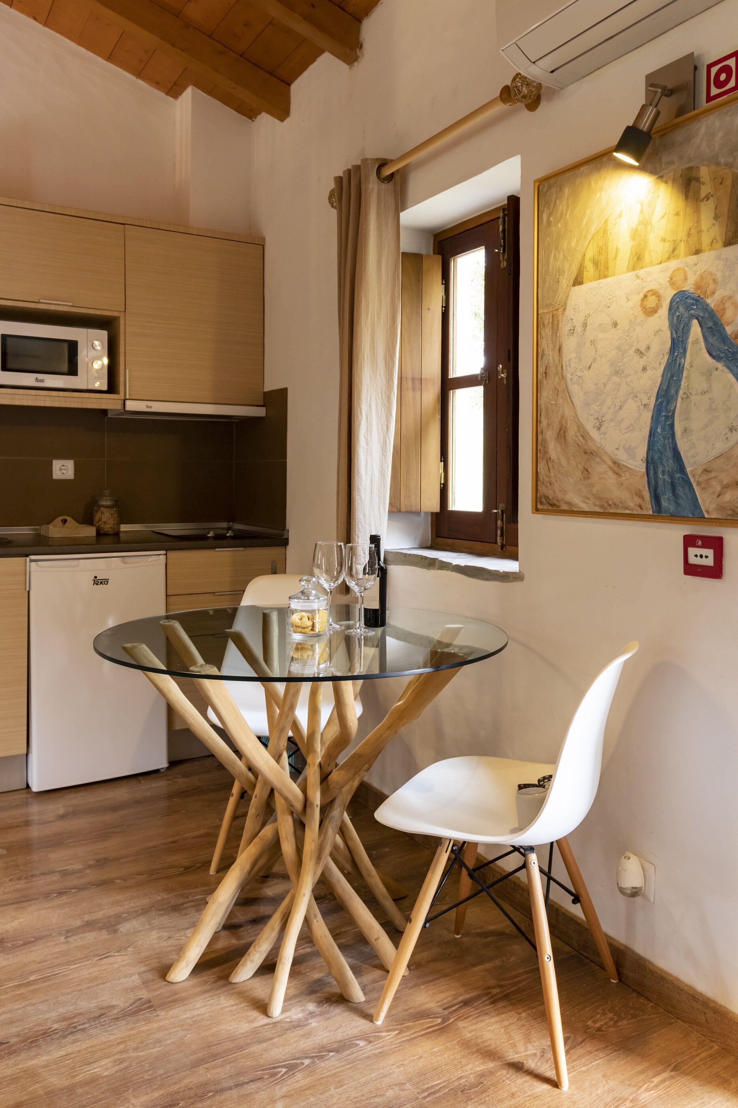 Una cocina compacta con una mesa de vidrio, sillas blancas y un refrigerador pequeño.