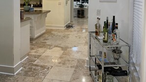 Un hall spacieux avec un coin cuisine sur la gauche, un coin repas avec une table et des chaises, et un bar avec des bouteilles et des verres sur la droite.