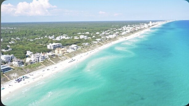 Vue aérienne d’une ville côtière avec une longue plage, des bâtiments le long du rivage et des eaux turquoise et limpides.