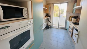 Een compacte keuken met een magnetron, oven en een schuifdeur naar een balkon.