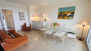 Een woonkamer met een glazen eettafel, witte stoelen, een bruine bank en een witte kast.