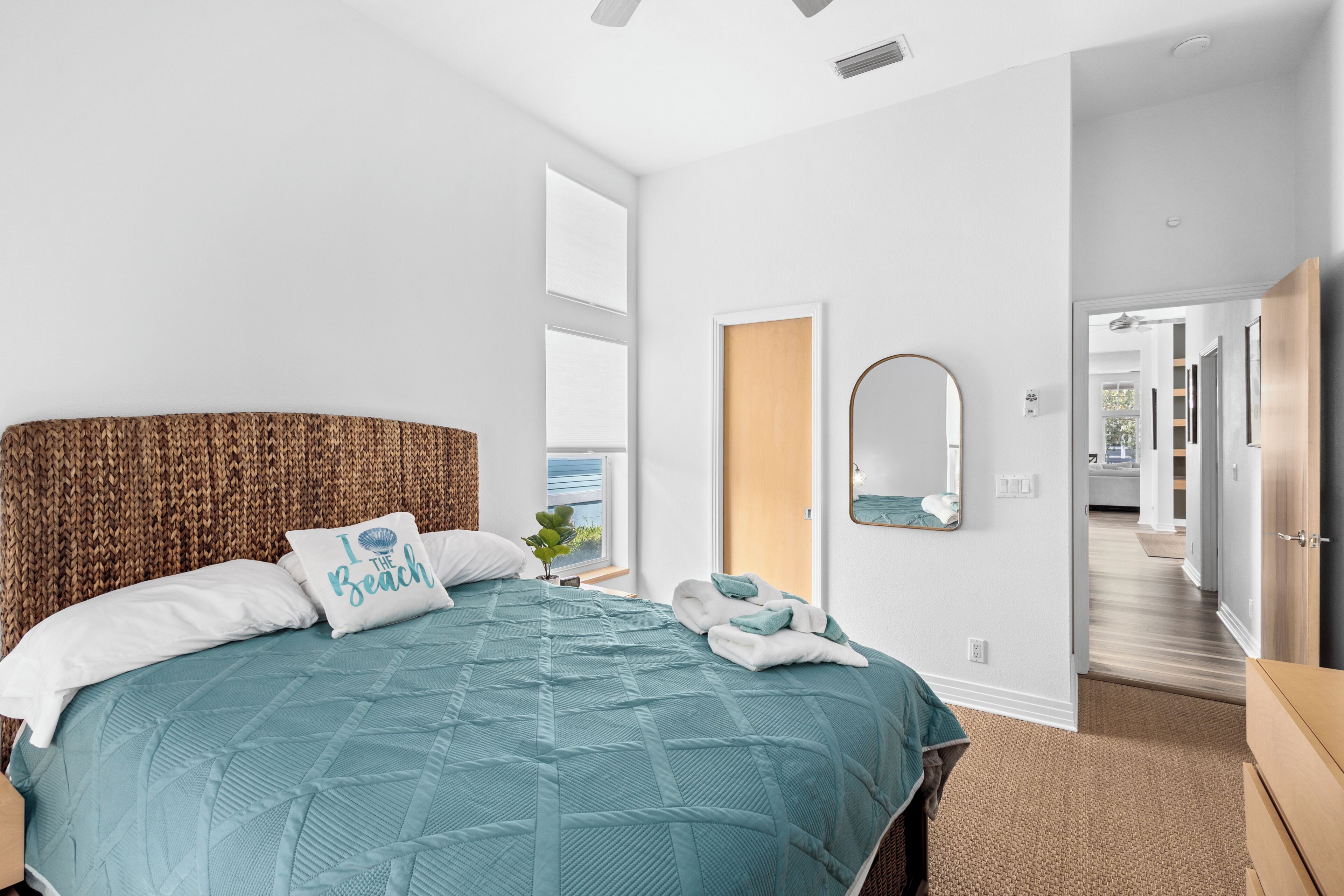 Ein Schlafzimmer mit einem großen Bett, einem Kopfteil, einem an der Wand befestigten Spiegel und Blick ins Freie.