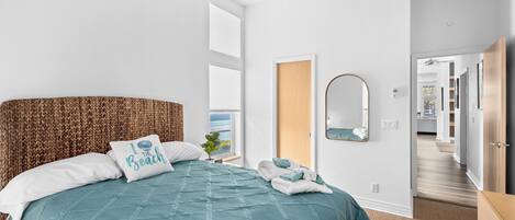 Ein Schlafzimmer mit einem großen Bett, einem Kopfteil, einem an der Wand befestigten Spiegel und Blick ins Freie.