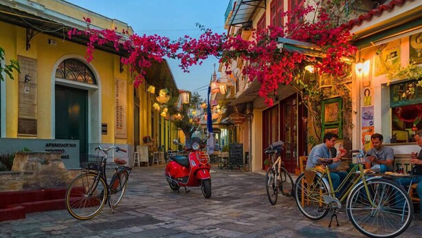 Una calle estrecha flanqueada por edificios, bicicletas estacionadas a lo largo de la acera y personas cenando en mesas al aire libre.