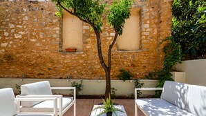 Un patio con mobiliario blanco, un árbol y un muro de piedra.