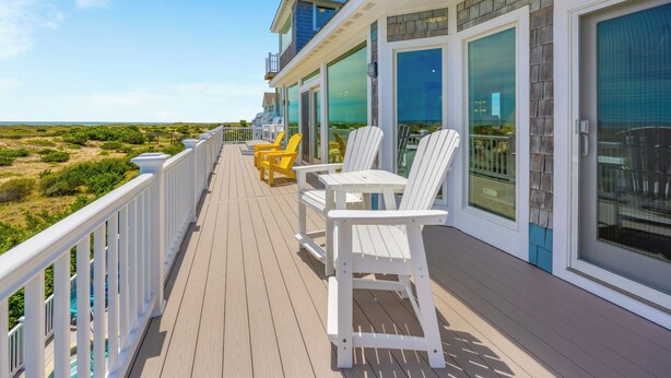 Une terrasse avec des chaises Adirondack blanches et une table, donnant sur une plage et des dunes.