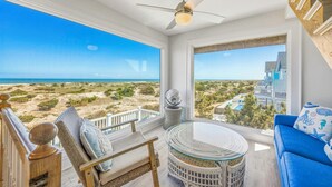 Un balcon avec vue sur la plage et l’océan, une chaise en osier, une table ronde en verre et un canapé bleu.