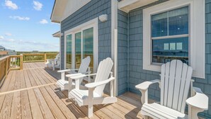 Una terraza de madera con sillas Adirondack blancas y un ventanal que da a un espacio cubierto.
