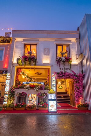 Un bâtiment avec une enseigne indiquant la présence d’un restaurant, des arrangements floraux à l’extérieur et un tapis rouge à l’entrée.