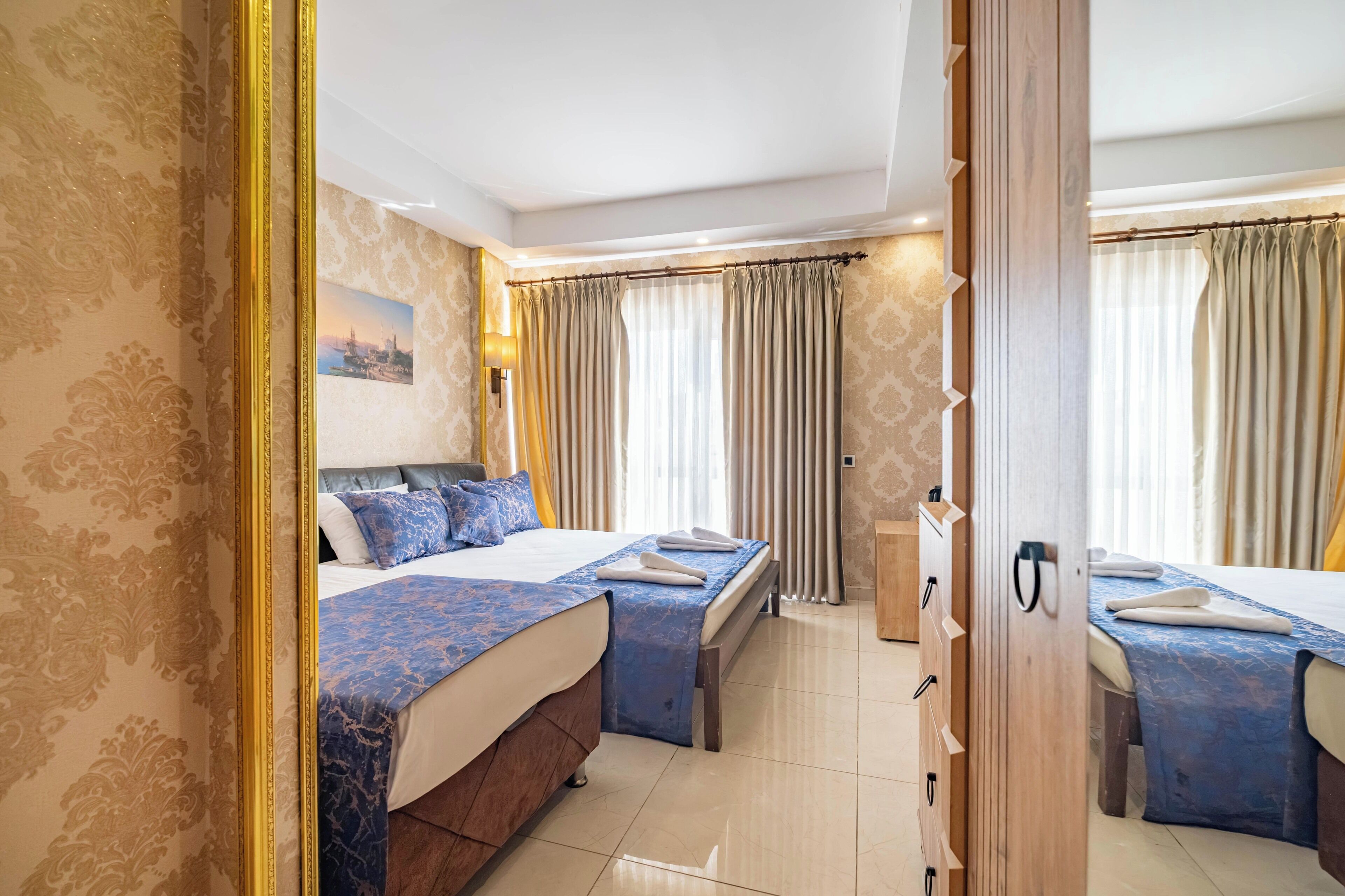 A hotel room with a large bed, a smaller bed, a wooden wardrobe, and a mirror.