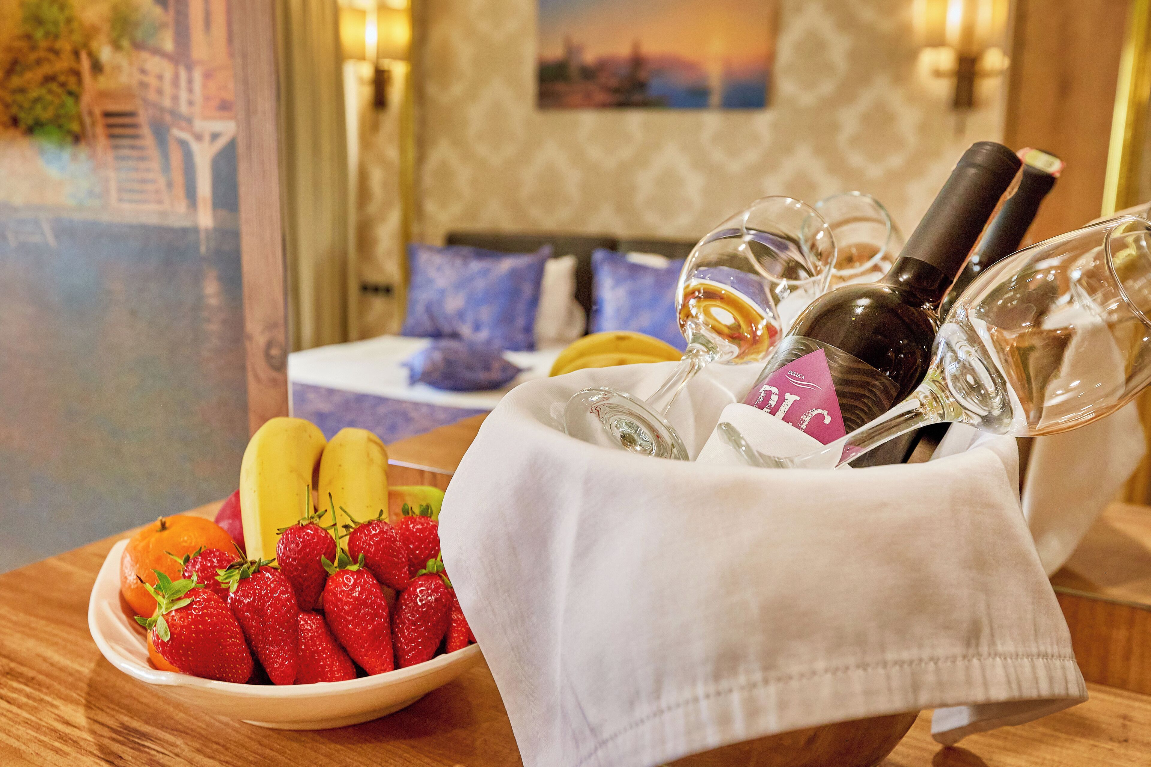 A table with a bowl of fruit, a bottle of wine, and wine glasses.