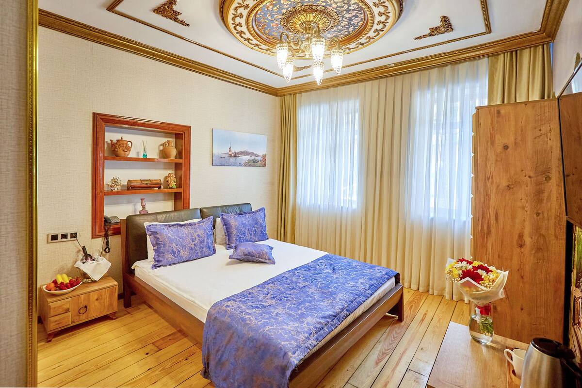 Habitación de hotel con una cama grande, cabecera de madera, una mesita de noche con lámpara, un armario de madera y un cuadro en la pared.
