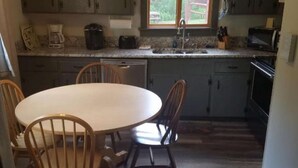 Een kleine keuken met een ronde eettafel, houten stoelen en donkerhouten kastjes.