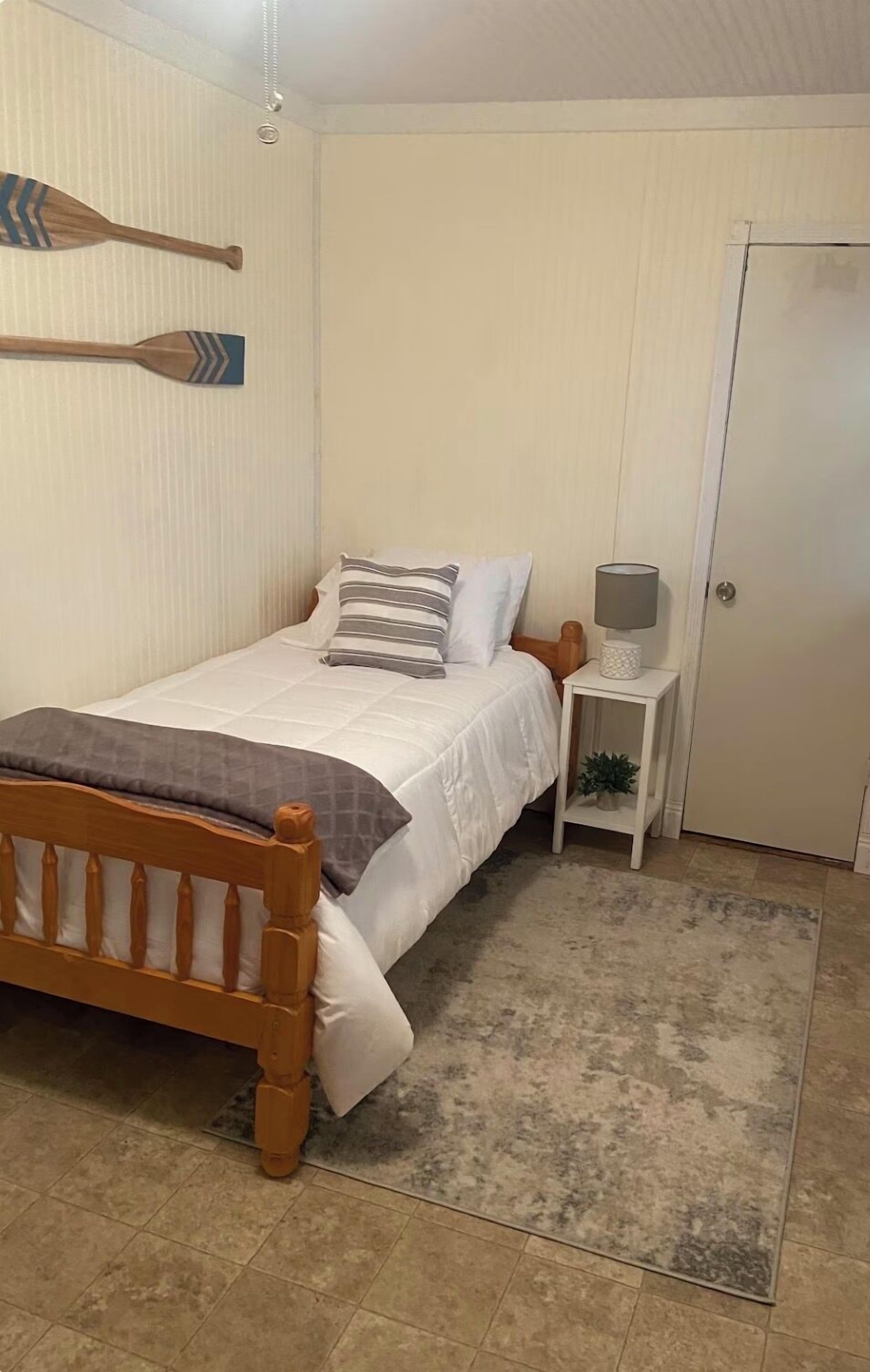 A bedroom with a wooden bed, white bedding, a small bedside table with a lamp, and a door.