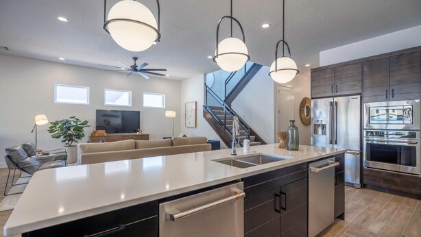 Une cuisine moderne dotée d’un grand îlot central, d’appareils électroménagers en acier inoxydable et de luminaires suspendus.