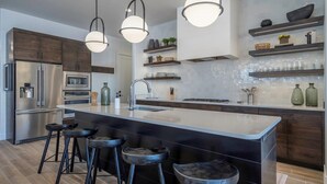 Une cuisine moderne dotée d’un grand îlot central, d’appareils électroménagers en acier inoxydable et de tabourets de bar.