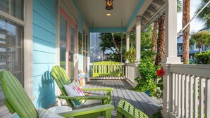 A porch with green chairs and a bench, a white railing, and a view of the street. - Updated Kitchen & Large Pool– Seacrest Simplicity Meets Coastal Comfort (Inlet Beach)
