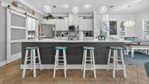 A modern kitchen with white cabinets, a dark gray island with bar stools, and pendant lighting. - Updated Kitchen & Large Pool– Seacrest Simplicity Meets Coastal Comfort (Inlet Beach)