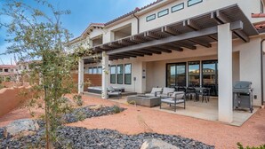 Une maison moderne dotée d’un patio aménagé avec des meubles d’extérieur, un barbecue et une pergola.
