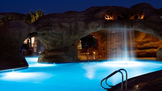 Une piscine agrémentée d’une cascade, entourée de grandes formations rocheuses.