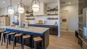 Une cuisine moderne dotée d’un îlot central, de tabourets de bar, de luminaires suspendus et d’appareils électroménagers intégrés.